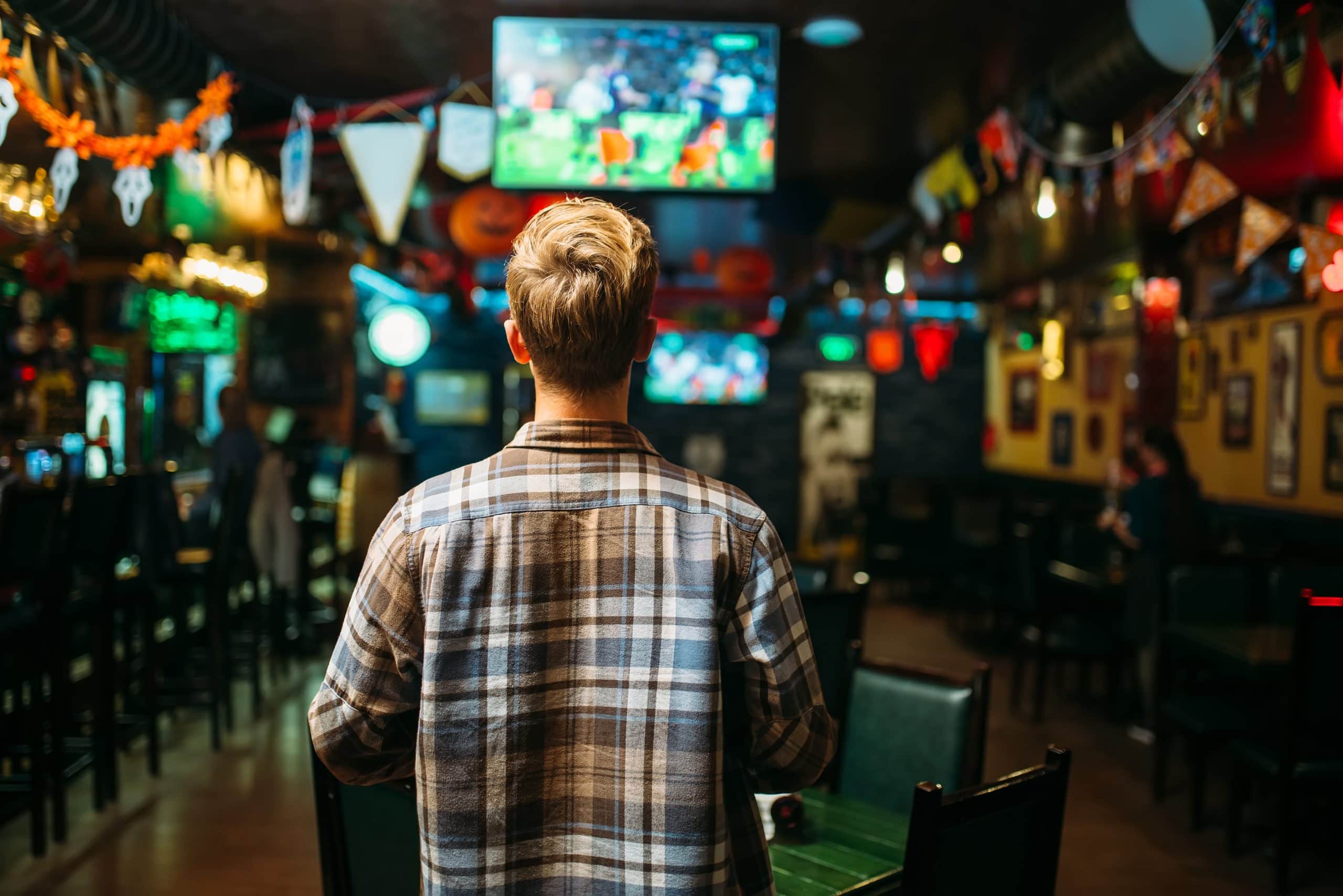 Football fan watching the match of the favorite team in sports bar, back view. Tv broadcasting of the game in pub